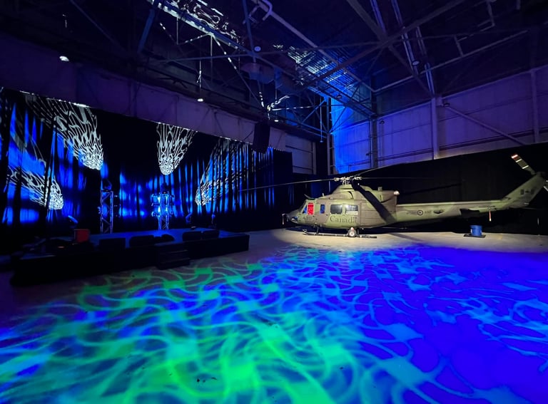 Military helicopter in a hangar with dramatic blue and green stage lighting and projections.