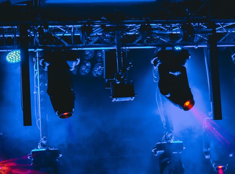 Professional stage lighting rig with spotlights and blue atmospheric haze for a concert event.