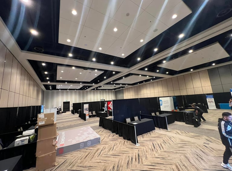 A large conference hall being set up with exhibitor booths, black drapery, and trade show displays.