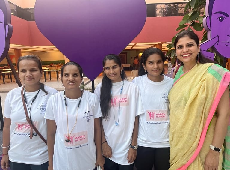 A group of low vision and blind girls smile at the camera along with Shruti with Purple Fest in back