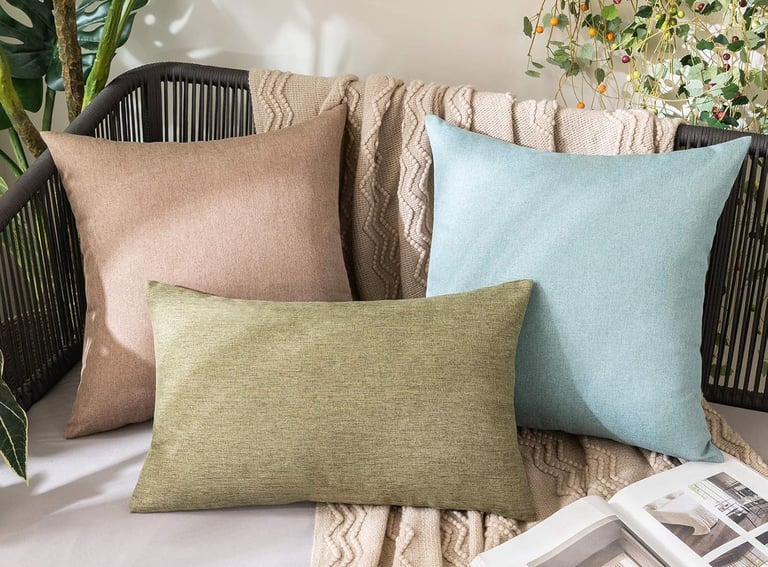 Decorative throw pillows in sage green, tan, and light blue on a stylish outdoor patio chair with a cozy blanket.