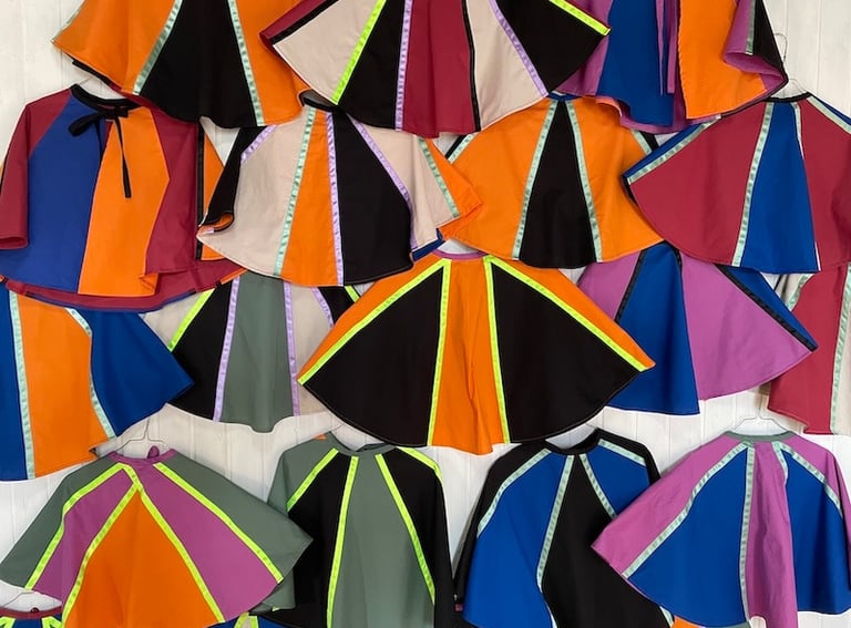 Collection of colorful handmade capes in vibrant block patterns and neon stripes for kids costumes.