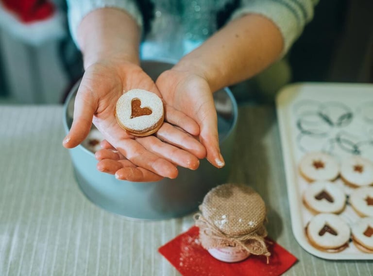Manos sosteniendo una galleta Linzer en forma de corazón con azúcar glas,