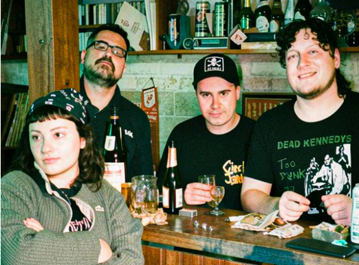 A group of young punk rock fans wearing band t-shirts sitting at a bar with drinks.