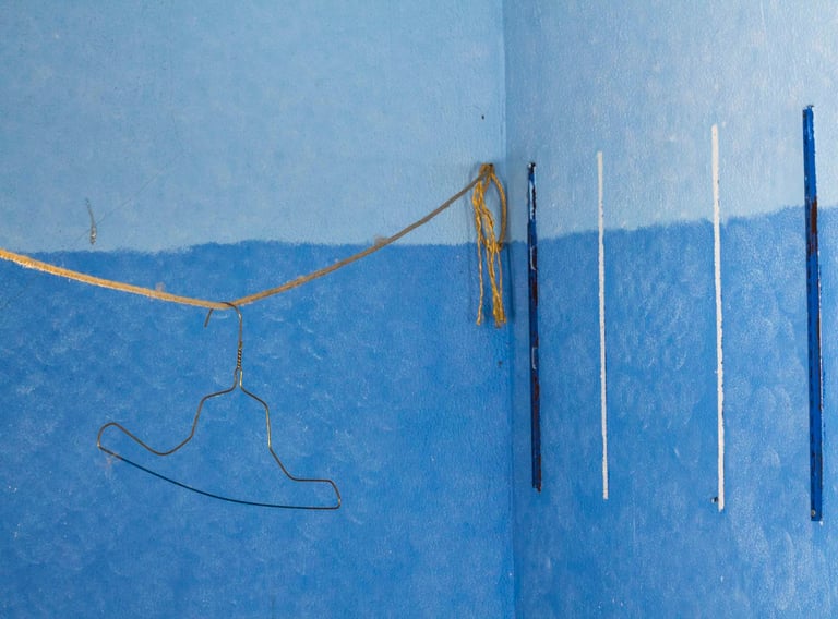 Golden bent clothing hanger dangling from a rope in a blue painted room. 