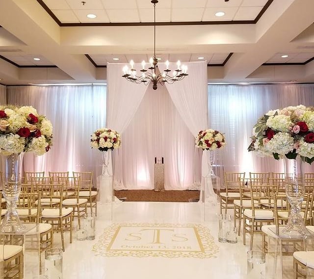 a wedding ceremony with a white aisle, uplights and lighting with gold chairs and white drapes