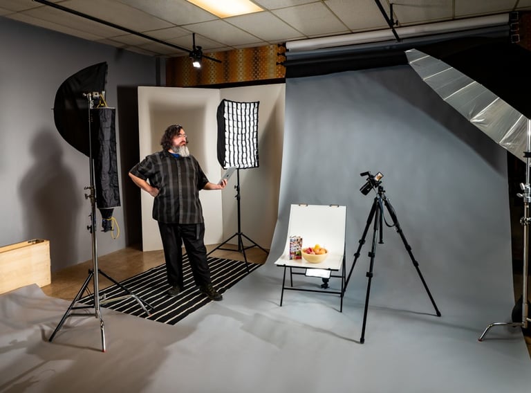 Man standing in a photo studio with equipment including lights, a backdrop, and a camera on a tripod