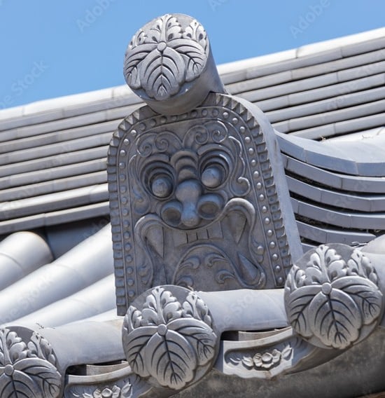 Ornate grey Oni-gawara roof tile with a carved demonic ogre face on a traditional Japanese temple.