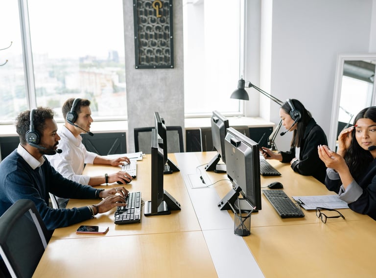 Smiling customer service representative wearing a headset, sitting at a desk with a computer