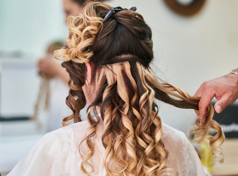 Estilista profesional aplicando extensiones rubias rizadas a una clienta para un peinado de boda.v