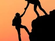 two people climbing a mountain at sunset