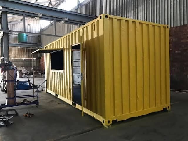 Yellow converted shipping container modified with a side window and door for an office or pop-up shop.