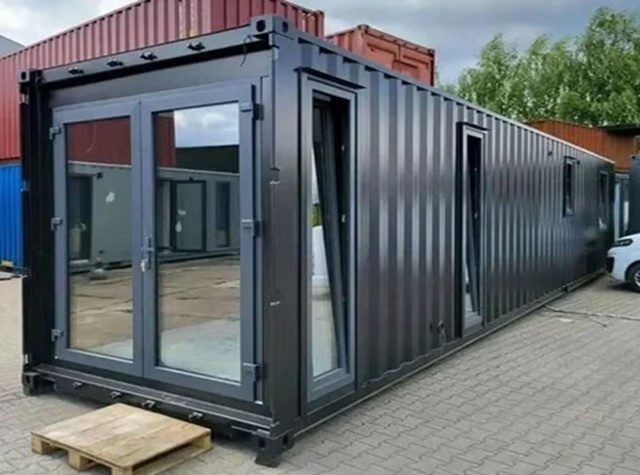 Modern black shipping container home with glass doors and windows on a paved lot.