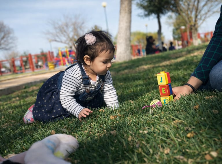 Una niña pequeña jugando con bloques de letras de colores sobre el césped en un parque