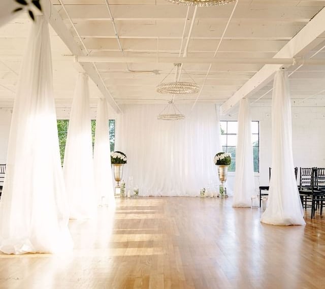 a room with a lot of white curtains and a chandelier; pipe and draping for event