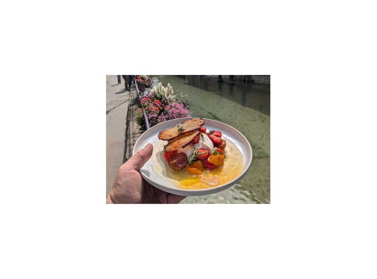 Une personne tient une assiette avec une burratta accompagné de fraises, tomates et un croustillant