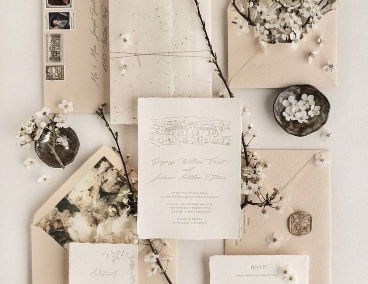 a wedding invitation suite with a floral arrangement of flowers and a vintage envelope