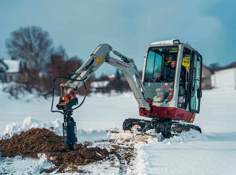 Excavator digging a post hole through frozen ground to reach the frost line for structural stability