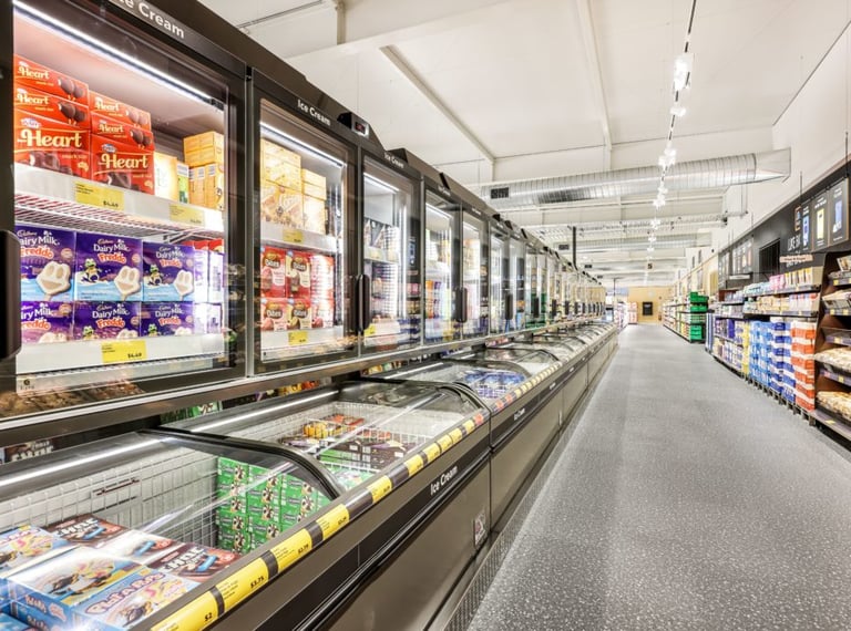 A wide grocery store aisle featuring a long row of glass-door ice cream freezers and frozen food displays.