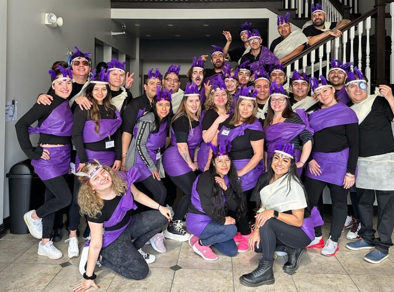 A large group of smiling people in matching purple and black costumes posing together in a lobby.