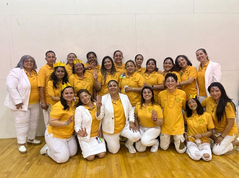 A diverse group of cheerful people wearing yellow shirts and white pants posing for a team photo.