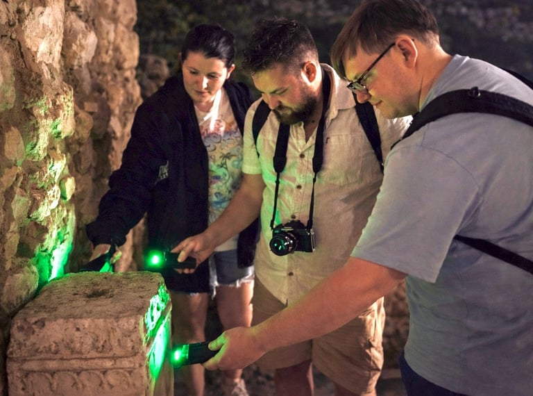 Tour participants examining ancient stone ruins with green UV lights during Athens Ghost Tour