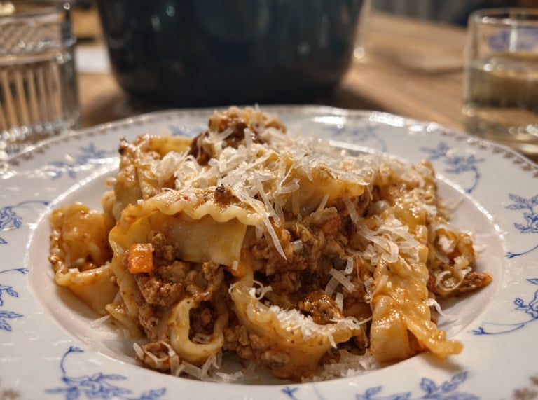 Traditional mafaldine pasta with savory bolognese meat sauce and grated parmesan cheese on a vintage floral plate.