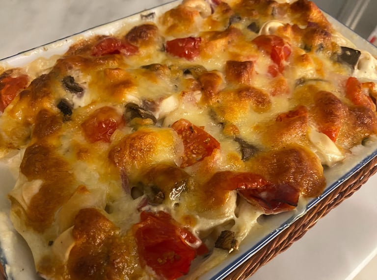Baked pasta casserole with melted bubbly golden cheese, fresh cherry tomatoes, and mushrooms in a ceramic dish.