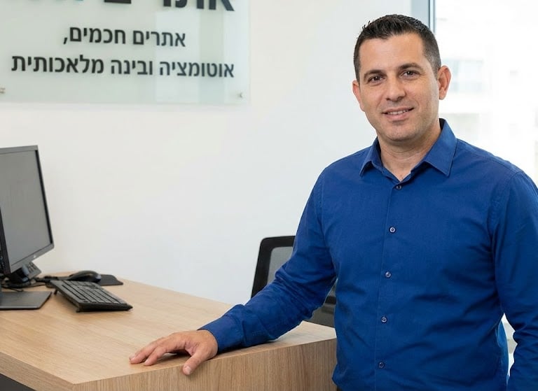 Professional man in blue shirt standing by office desk for AI and automation consulting services.
