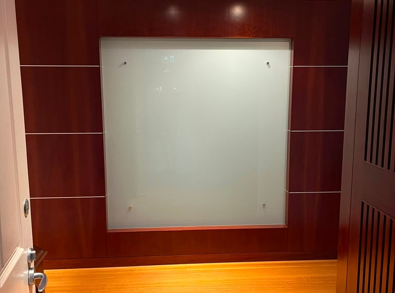 Modern office hallway featuring a frosted glass wall panel set in dark mahogany wood paneling with light oak floors.