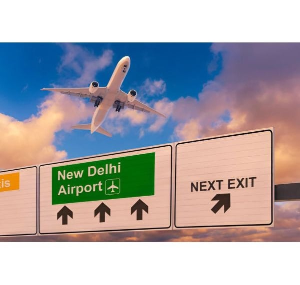 a plane flying over a highway sign new Delhi airport with a plane in the background
