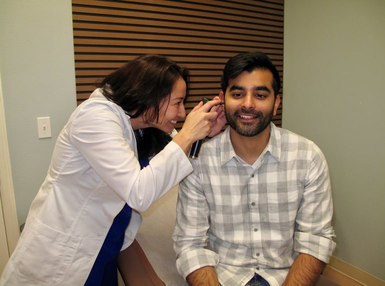 Dr Connolly uses an otoscope to perform an ear exam on a male patient in a clinic.