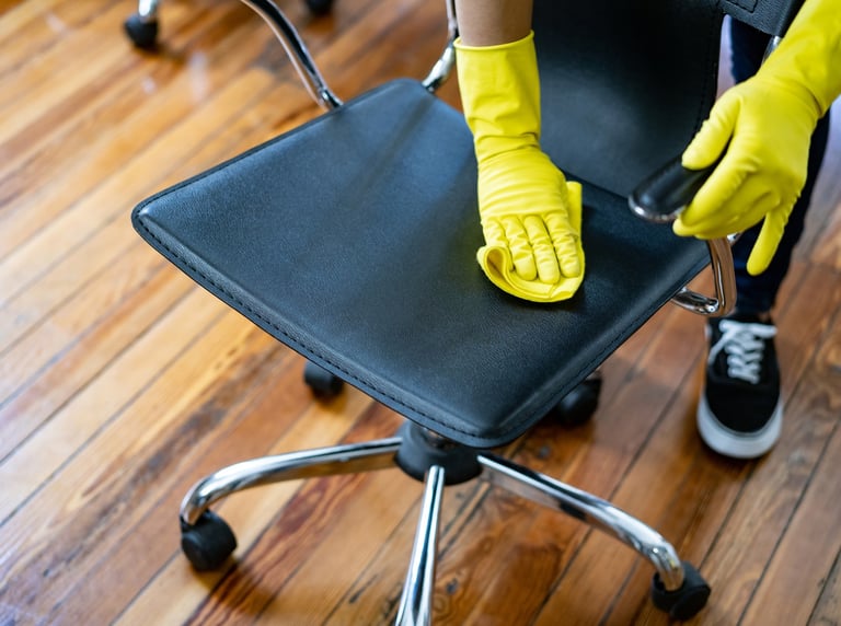 Person cleaning a black office chair with yellow gloves.