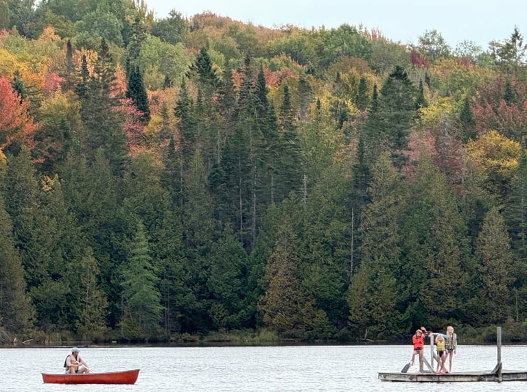 Three kids on a raft in the middle of a Vermont lake as their father looks on from a nearby canoe