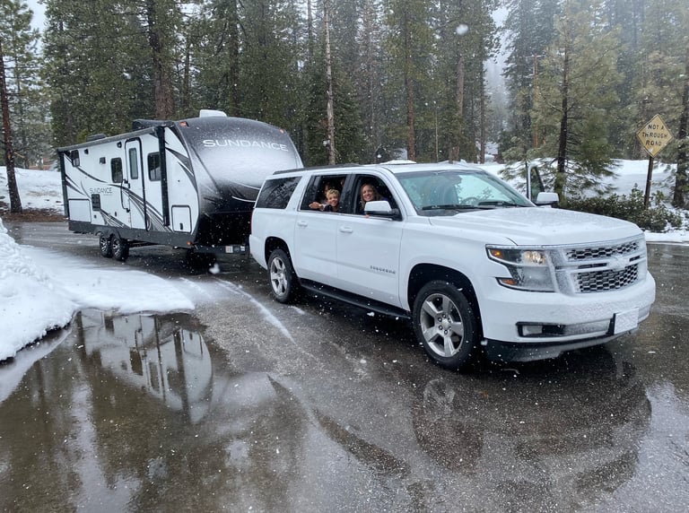 rv rental in the snow being towed behind a SUV with a big happy family in the windows
