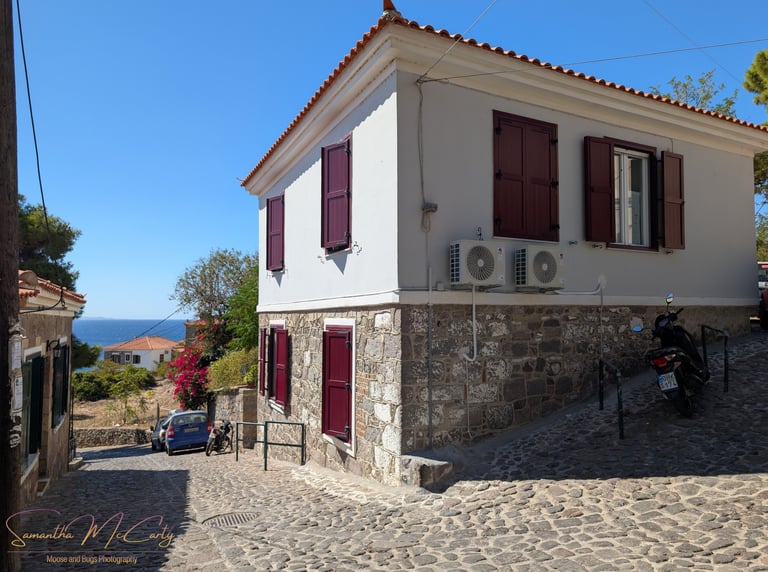 beautiful street view in Petra, Greece with cobblestone and white stucco wallls and burgundy shutter