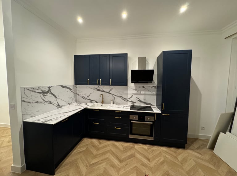  Réalisation d'une cuisine équipée avec plan de travail en marbre, meubles noirs et parquet chevron. Harenova