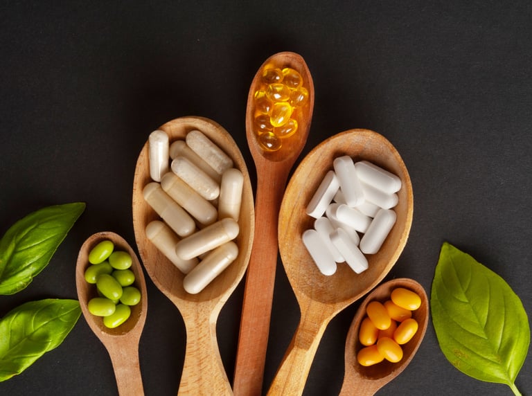 Variety of herbal supplements and vitamin capsules in wooden spoons on a dark background.