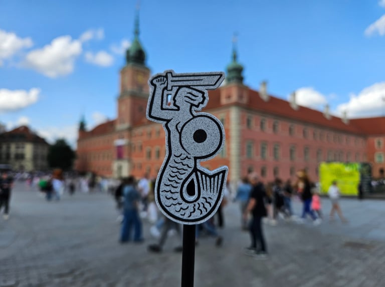 Magnes z Syrenką Warszawską na tle panoramy Placu Zamkowego