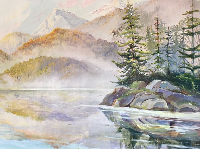 A forested island in front of foggy mountains reaching down to the shore.