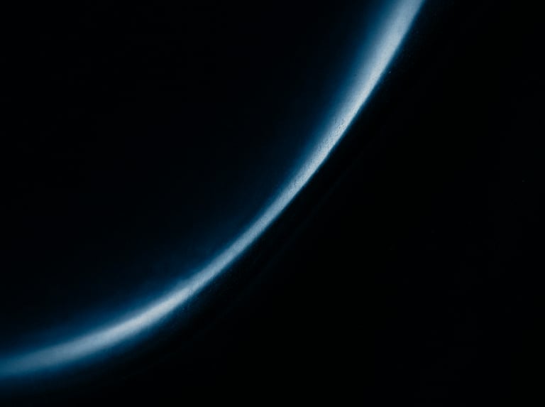 A dark, moody abstract photograph of light reflecting off a polished obsidian surface, creating soft blue gradients. Elegant, minimalist composition with an aura of exclusive anticipation.