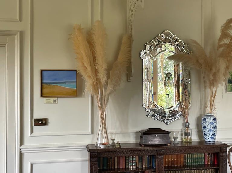 Elegant home decor featuring pampas grass in a glass vase, an ornate Venetian mirror, and a vintage bookshelf.