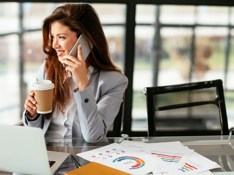 happy, productive realtor drinking coffee and on the phone at her desk