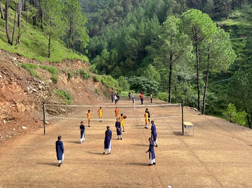 Section of bare earth carved out of mountain. Girls playing volleyball.side with