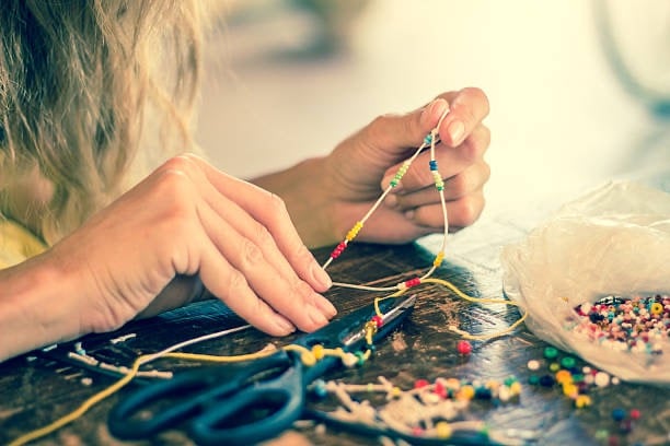 Close-up of hands crafting a handmade beaded necklace with colorful seed beads on a wooden table.