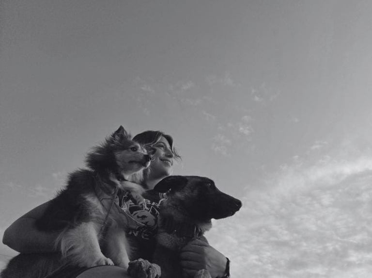 Mujer sonriendo mientras agraza a sus dos perros en un evento de educación canina 