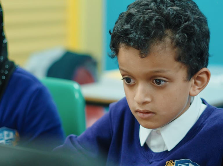 a boy is sitting at a desk with a laptop