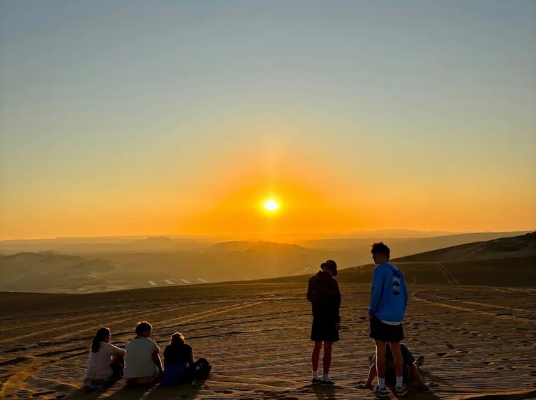A group of people with backs to camera in the desert watching the sunset