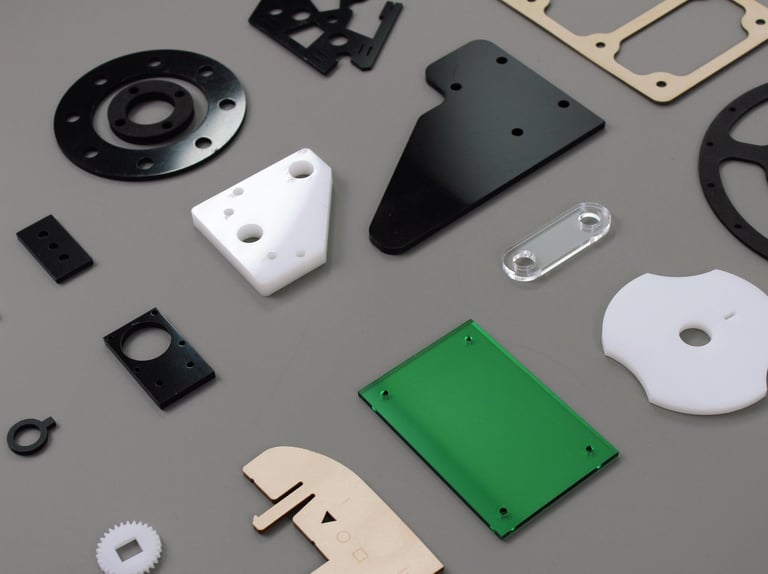Collection of precision laser cut plastic, acrylic, and wood industrial components on a gray surface.