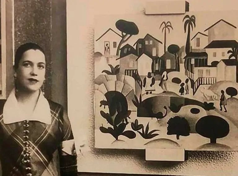 foto de Tarsila do Amaral, ao lado de uma quadro pintado por ela.